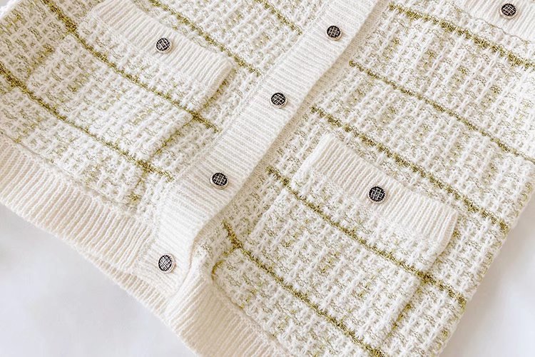 Close-up of a textured white fabric with gold accents and black buttons on a white background