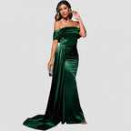 Woman in a green evening gown standing in front of a red couch against a dark background