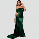 Woman in a green evening gown standing in front of a red couch against a dark background