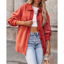 Person wearing an orange jacket, white top, and blue jeans outdoors.