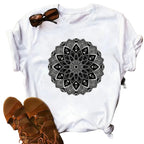 White t-shirt with black mandala design on a wooden surface with sandals and jeans.