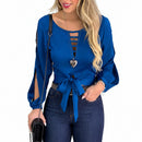 Woman wearing a blue top with cut-out design and tied waist, holding a black handbag.