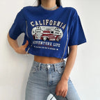 Person wearing a blue t-shirt with 'California Adventure Life' design and jeans on a white background