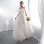 Woman in a white wedding dress holding flowers in a bright room with white curtains.