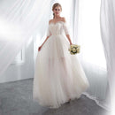 Woman in a white wedding dress holding flowers in a bright room with white curtains.
