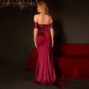 Woman in a burgundy evening gown standing in a dimly lit room with a red couch.