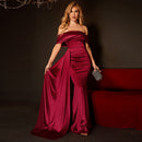 Woman in a burgundy evening gown holding a clutch in a dimly lit room.