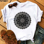 White t-shirt with black mandala design on a wooden surface with sandals and jeans.