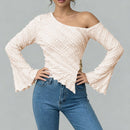 Woman wearing a beige off-shoulder top and blue jeans on a gray background